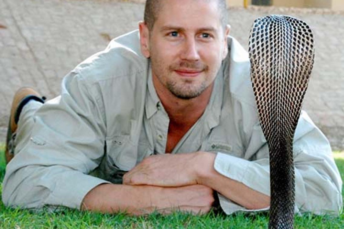 Associate Professor Bryan Fry flat on his stomach staring at a rearing cobra 