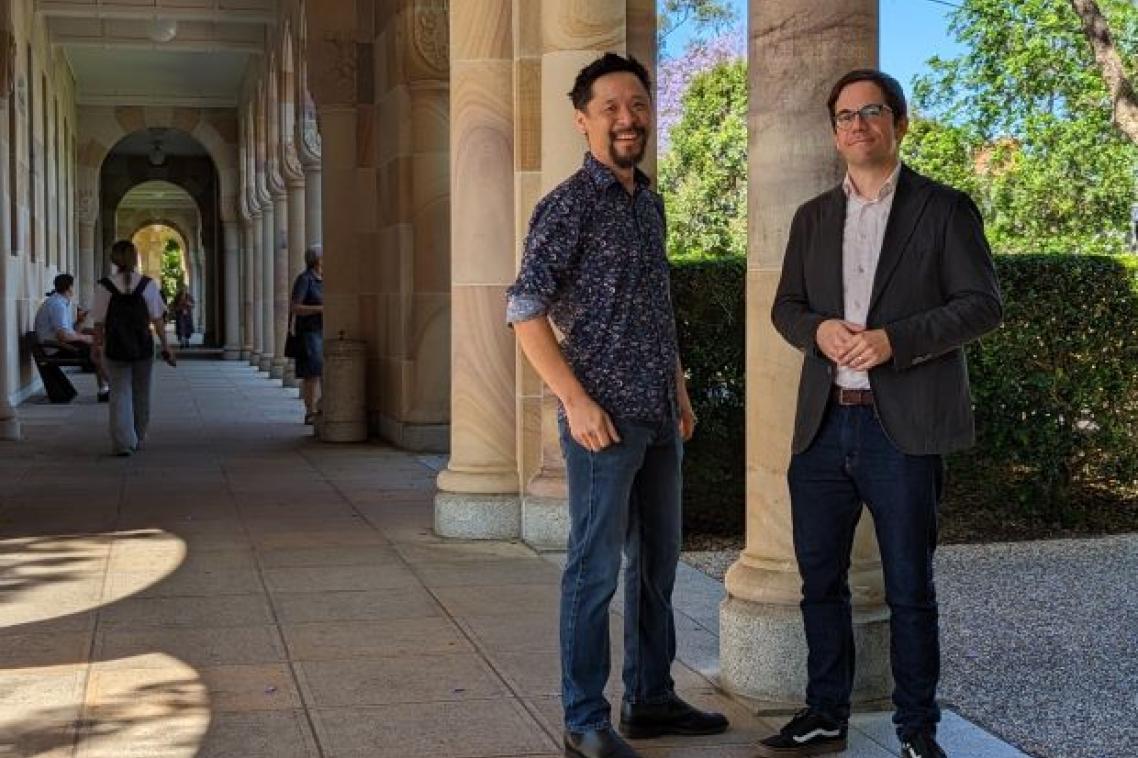 two men stand by a pillar in a shady stone walkway