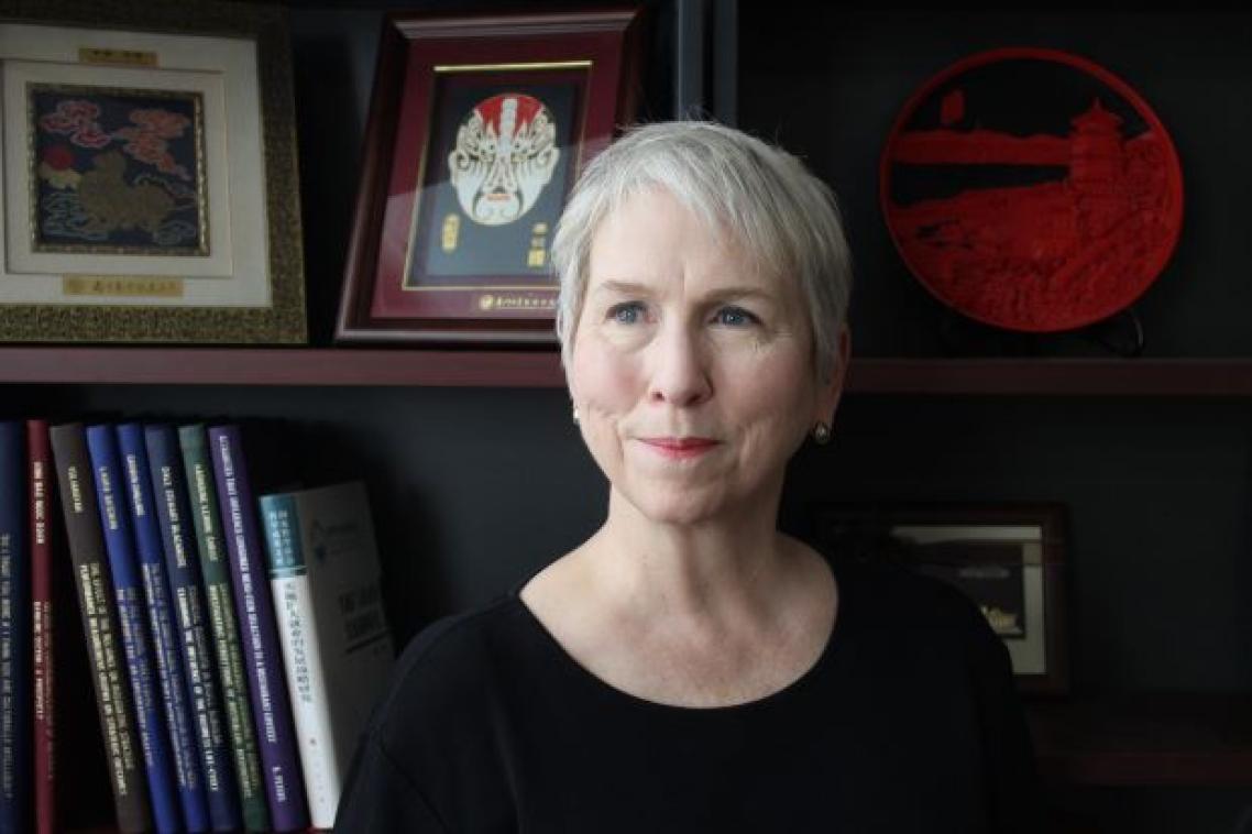 woman with short hair looks off camera, there is a bookshelf and framed images behind her
