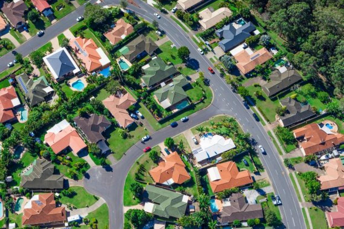 An aerial photo of a typical Australian suburb, showing roads, house rooftops, backyards and swimming pools.