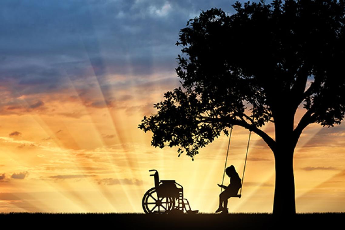 A silhouette image of a child on a swing under a tree with a wheelchair nearby.
