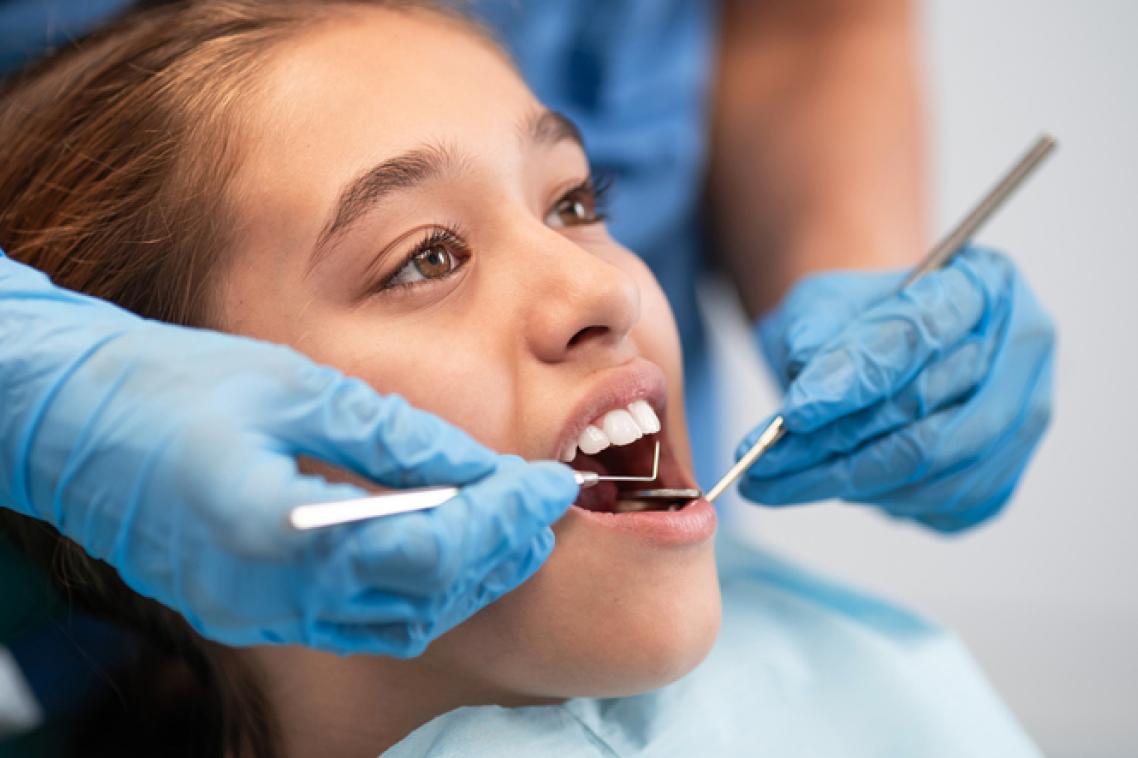 A young girl in close up as a dentist checks her teeth with instruments