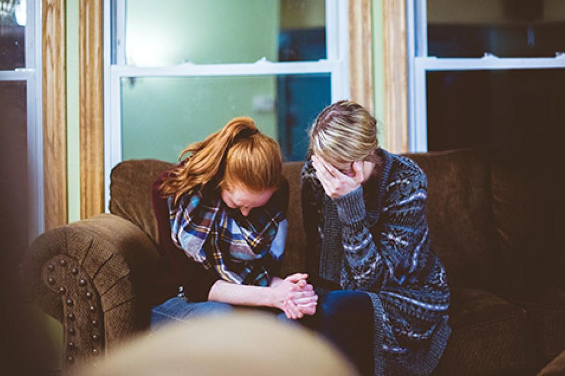 Two women sitting on a couch looking visibly upset