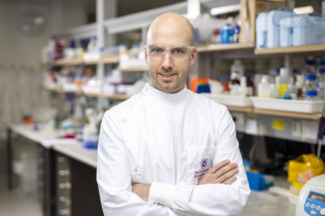 Head shot of Dr Dan Watterson with his arms folded across his chest, and the lab behind
