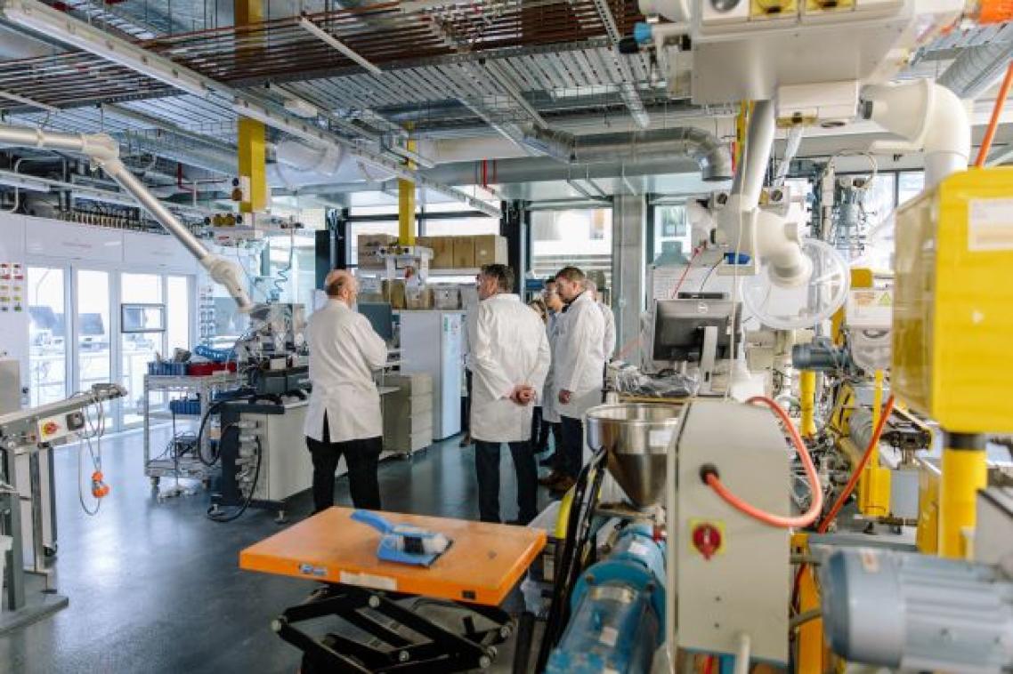 A group of people in white coats look at machinery inside a high-tech laboratory