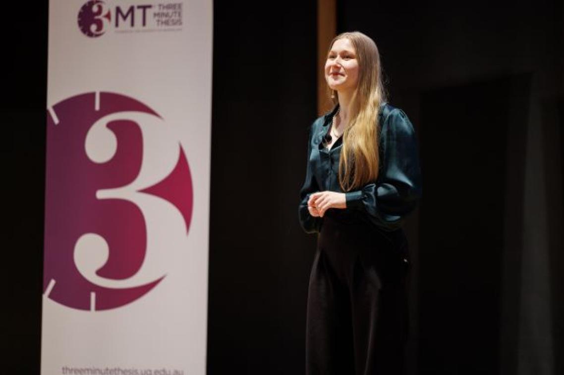 A woman with blonde hair wearing a green blouse and navy pants standing on a stage