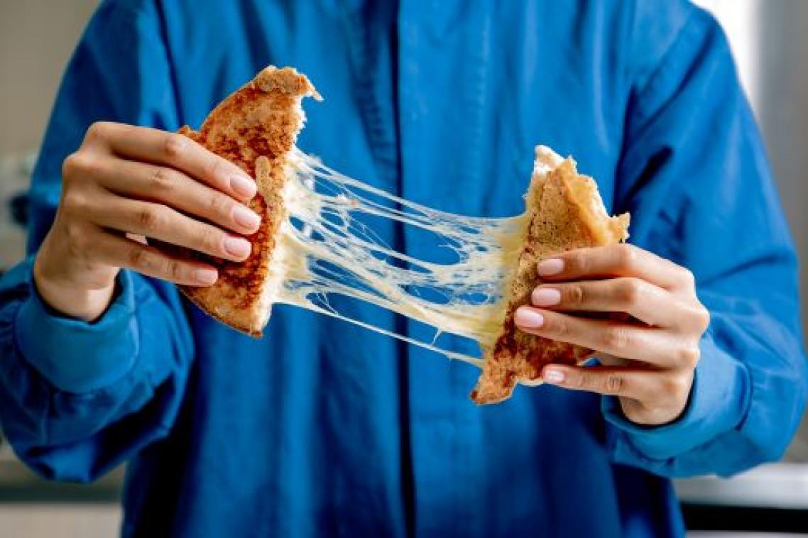 A person in a blue button-down shirt is pulling apart a toasted cheese sandwich, with strings of melted cheese between the two sides.