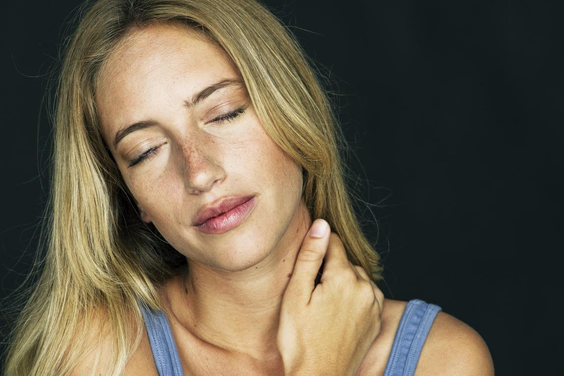A woman holds her neck in pain with her right hand.