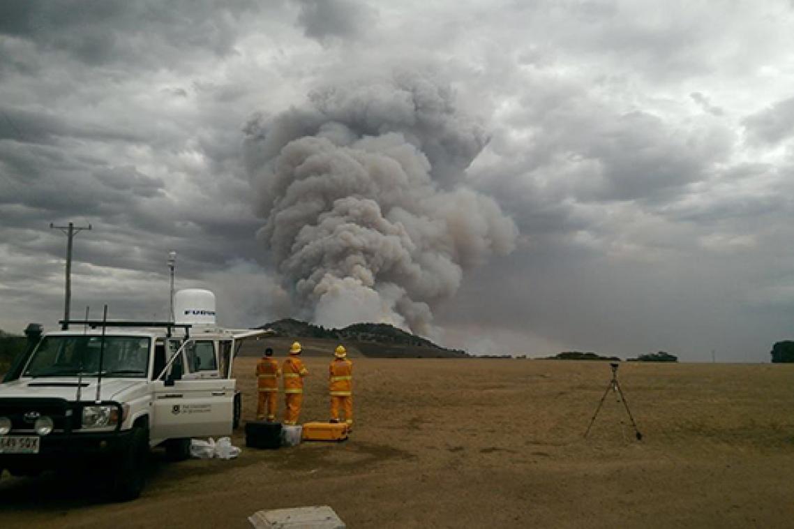 Firefighters standing near a truck watching a large plume of smoke.