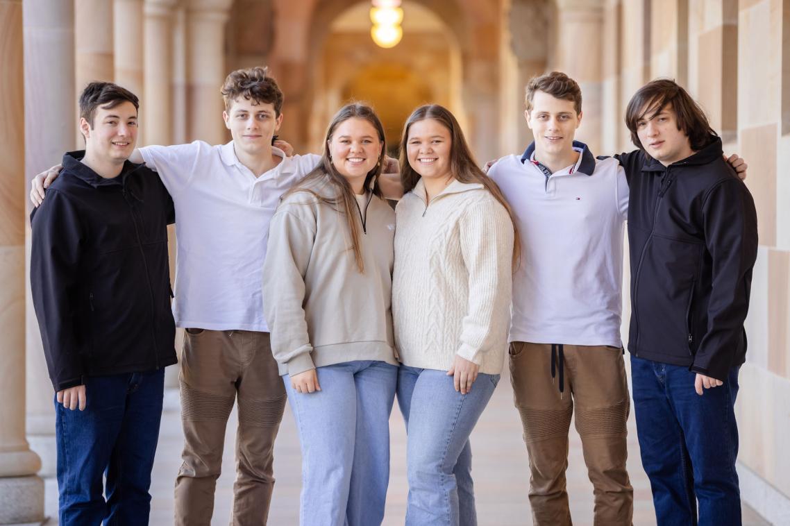 a group of six people stand in a corridor with their arms around each other