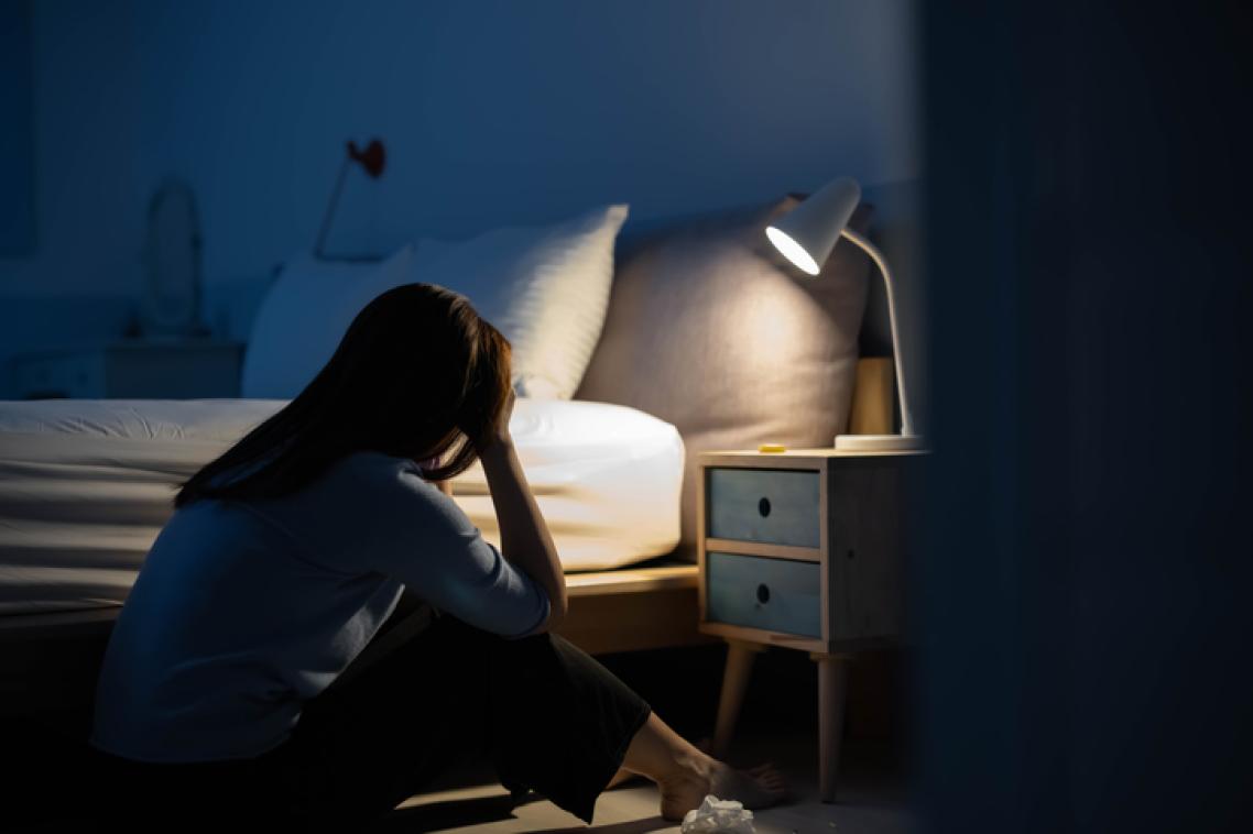 A teenage girl sitting with her head in her hands in a dark bedroom.