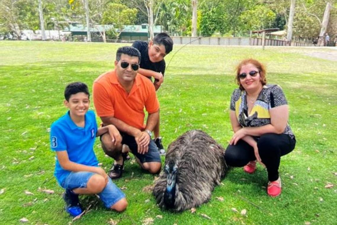 A man, woman and two boys pose on the grass next to a seated emu or ostrich at a wildlife park