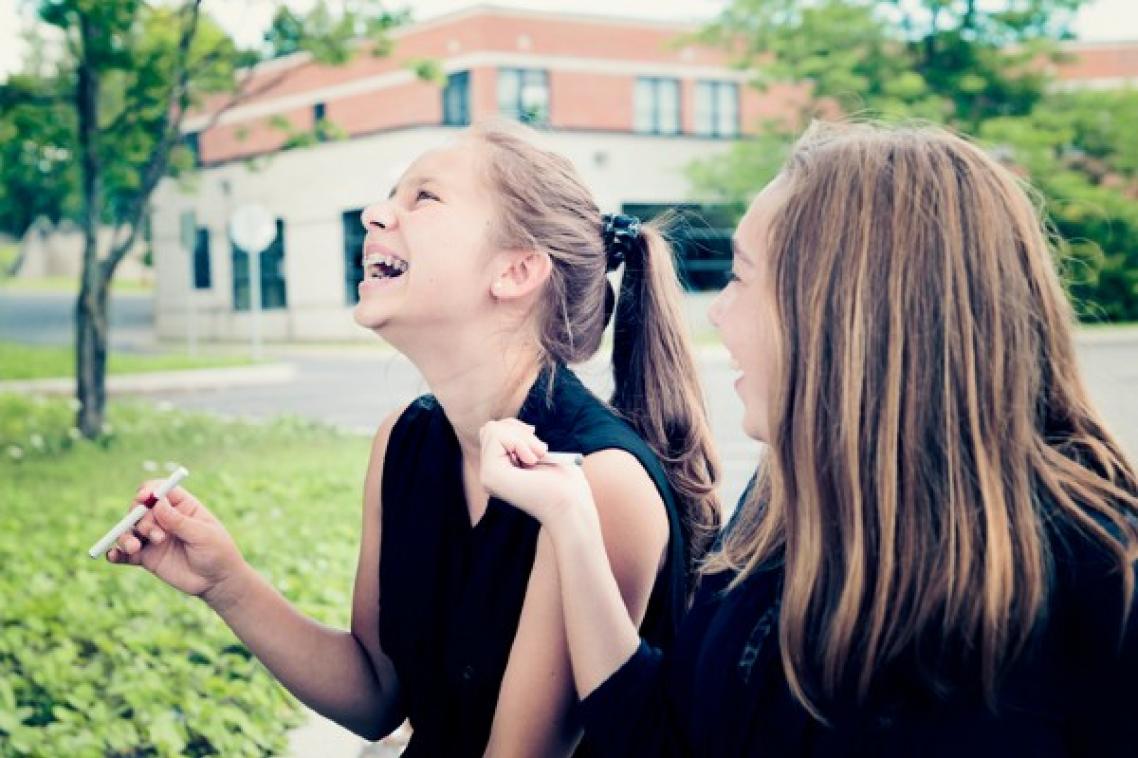 Young girls inhaling vape in park.
