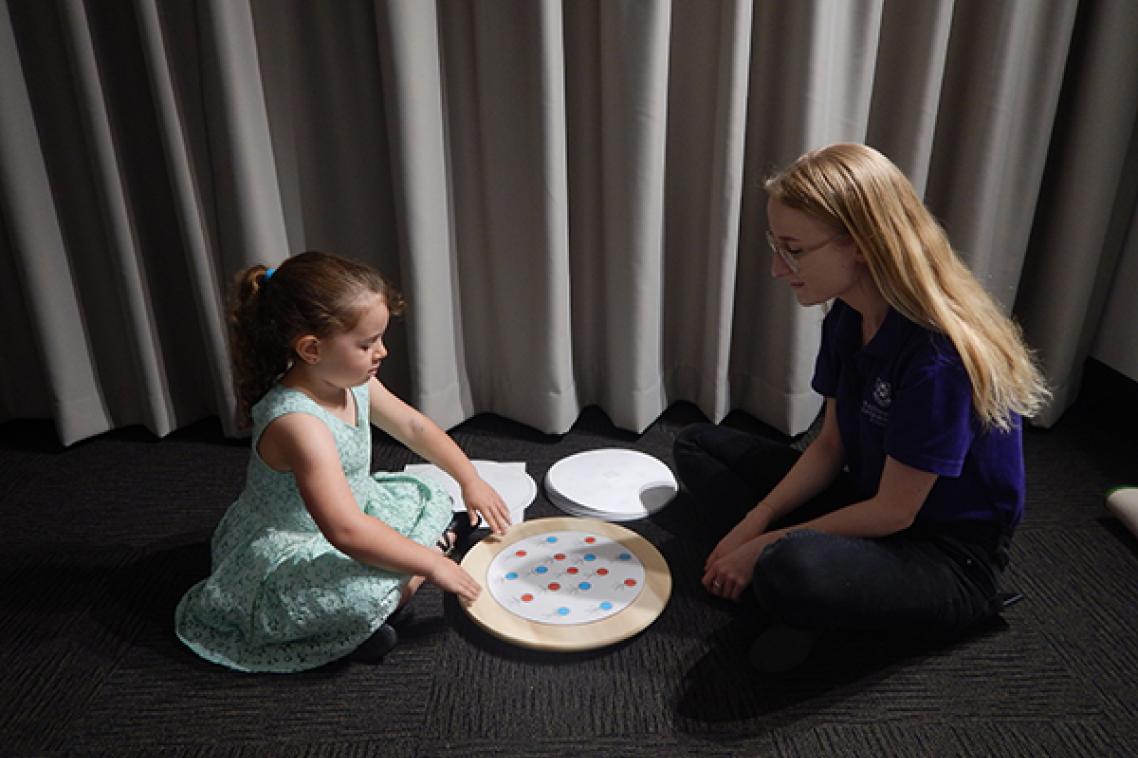 Young girl sitting with UQ PhD candidate manually rotating a turntable