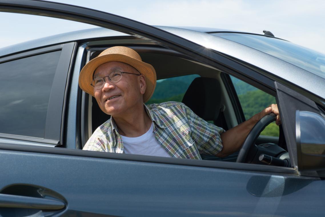 A man wearing a hat looks out the open door of a car.