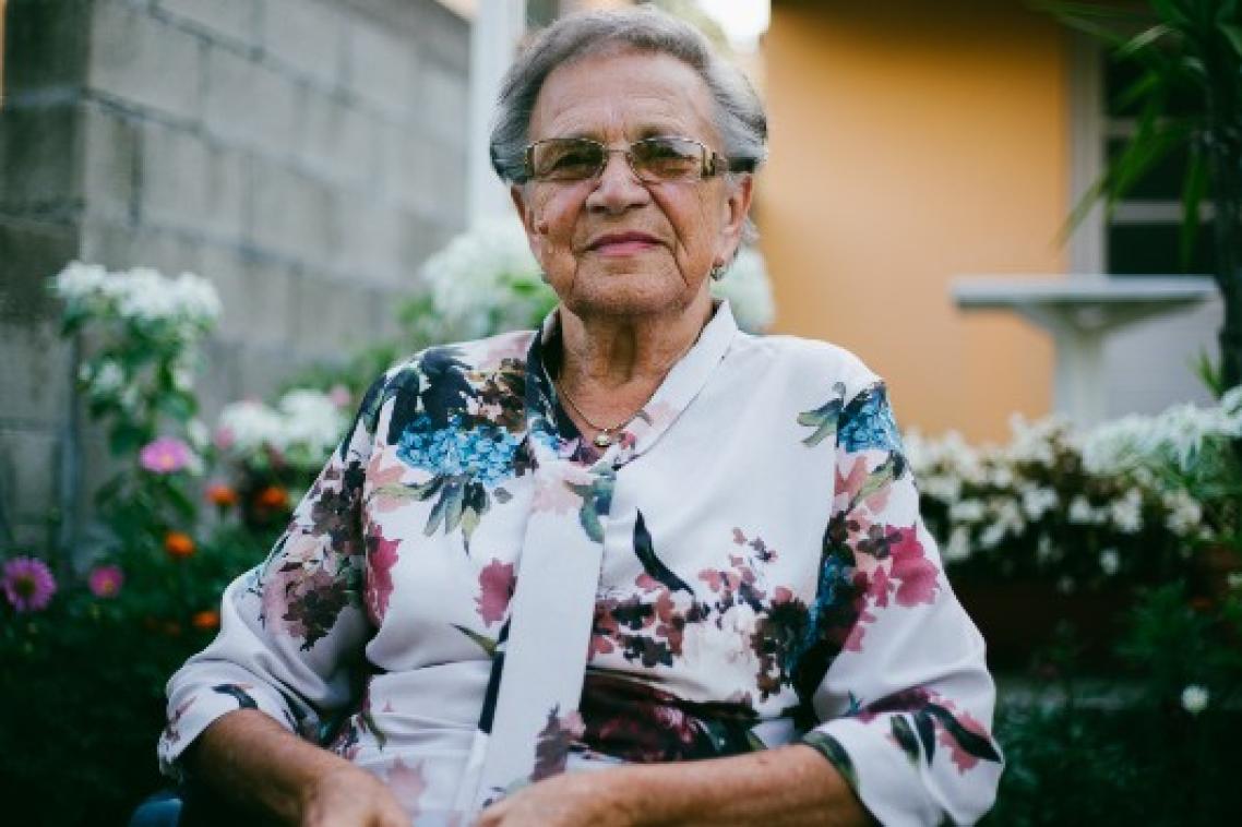 Elderly woman in floral shirt sits on walker.