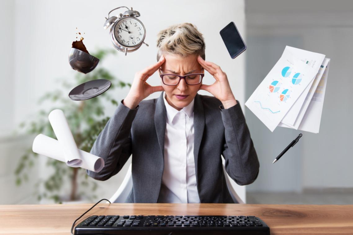 Image of a woman with hands to her temples with a phone, clock, spilling coffee cup and papers surrounding his head