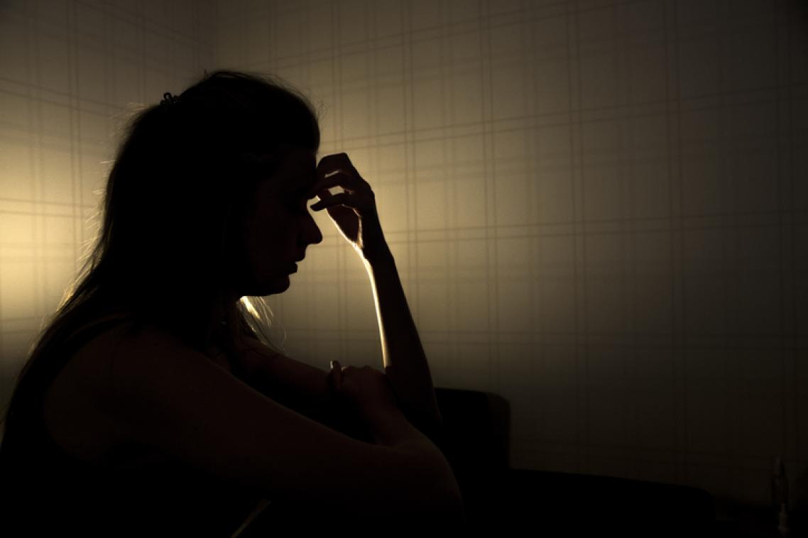 Woman in shadow with hand to forehead.