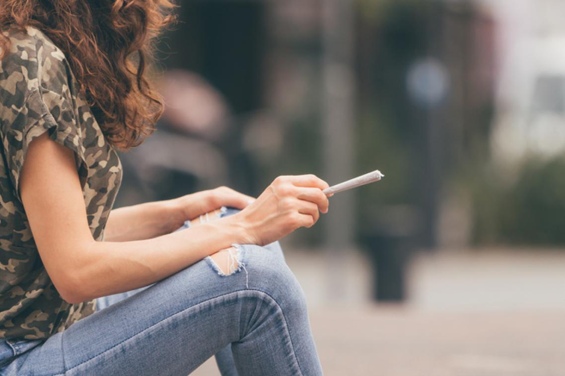 Image of a woman wearing jeans sitting down with a joint in her hands
