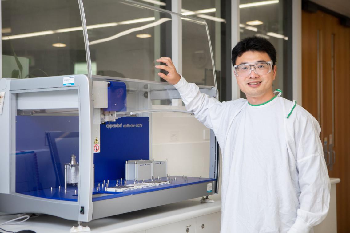 Dr Chun Xu in the laboratory with his hands on a piece of equipment