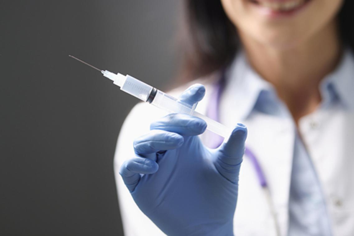 Close up of gloved woman's hand holding a syringe, with her trunk blurred in the background.