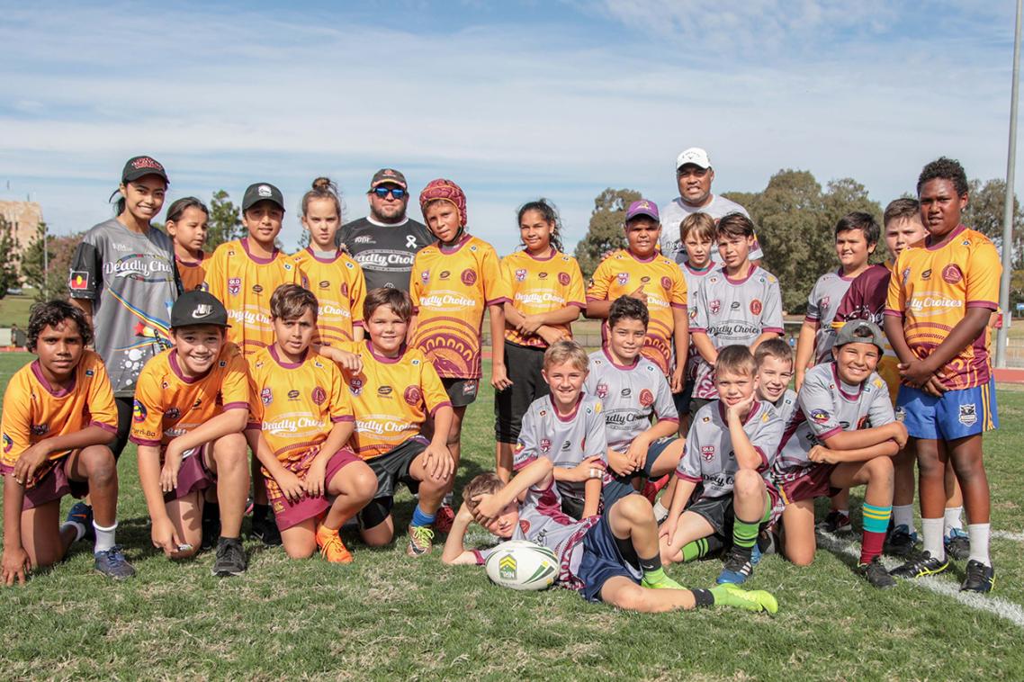 A group of young Aboriginal and Torres Strait Islander boys pose in yellow rugby uniforms. They are smiling.