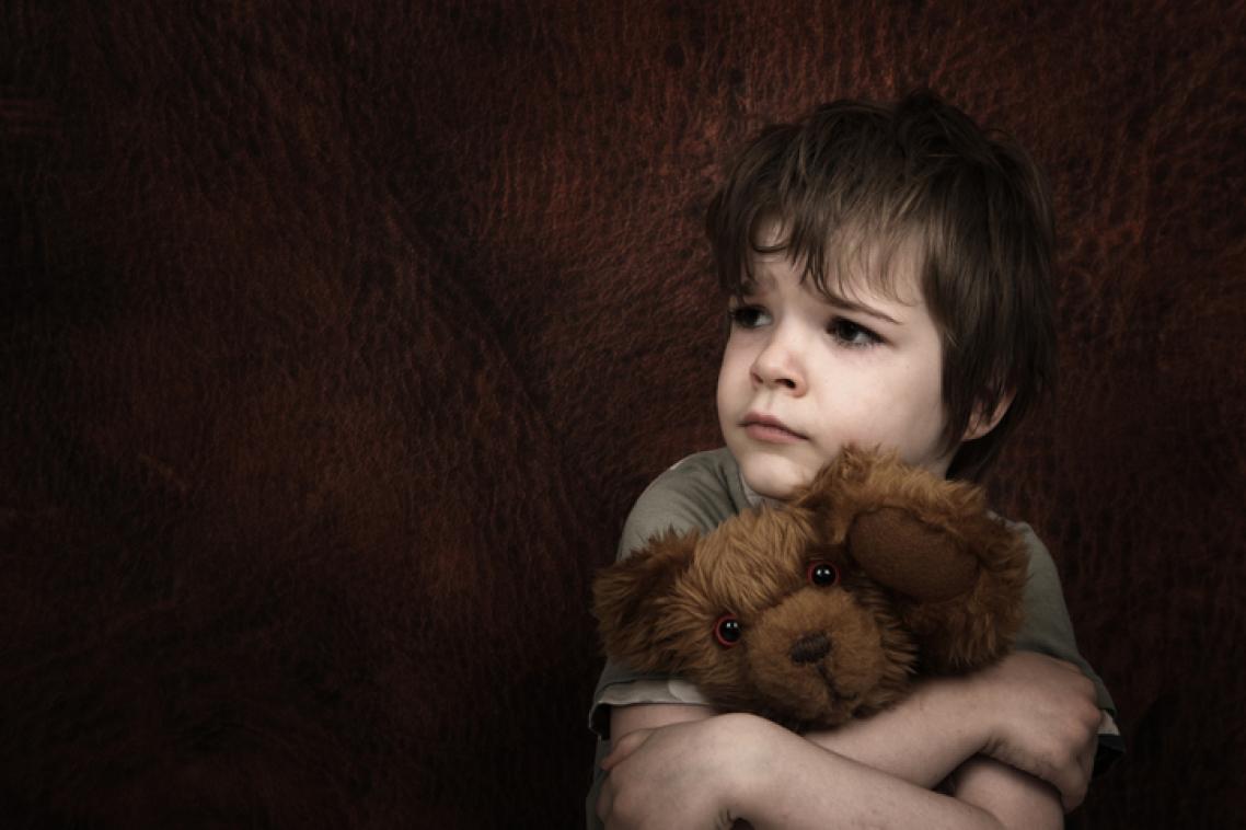 Young child looking distressed and holding teddy bear.