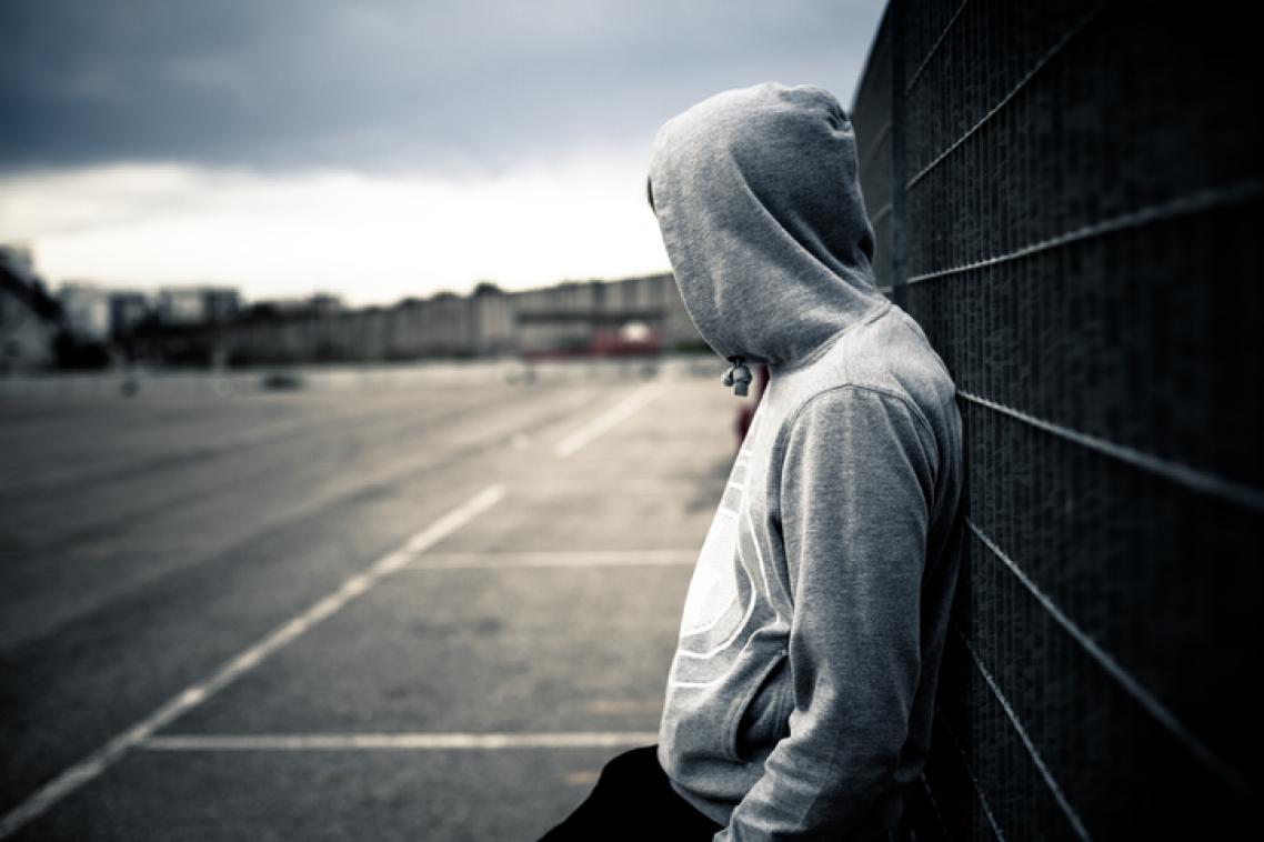 A teenager wearing a hoodie leans against a wall.