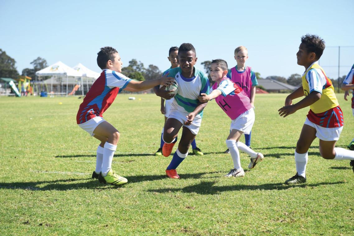 Young boys on a field playing rugby league, with a player being tackled