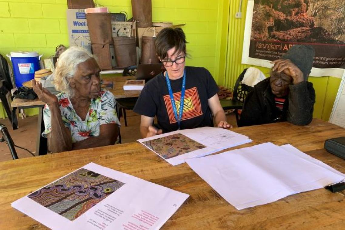 Three people sitting at a table looking at book.