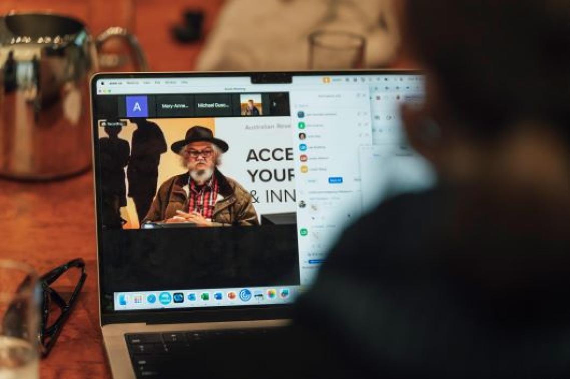 An image showing a laptop screen over a person's shoulder, with an Indigenous Australian on the screen.