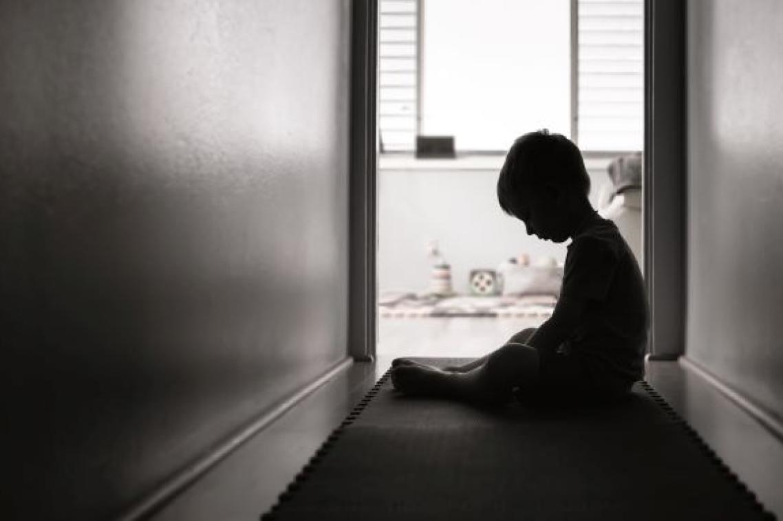 Child sitting in darkened hallway with head down. Adobe
