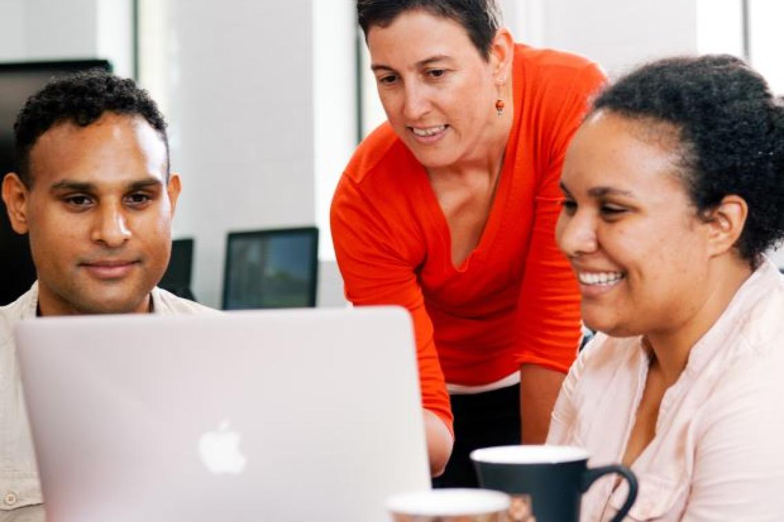 Two university students looking at laptop while lecturer looks over their shoulder. Image, UQ