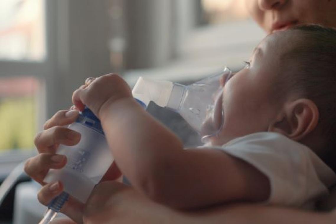 Child lying on bed with nebuliser mask on face.