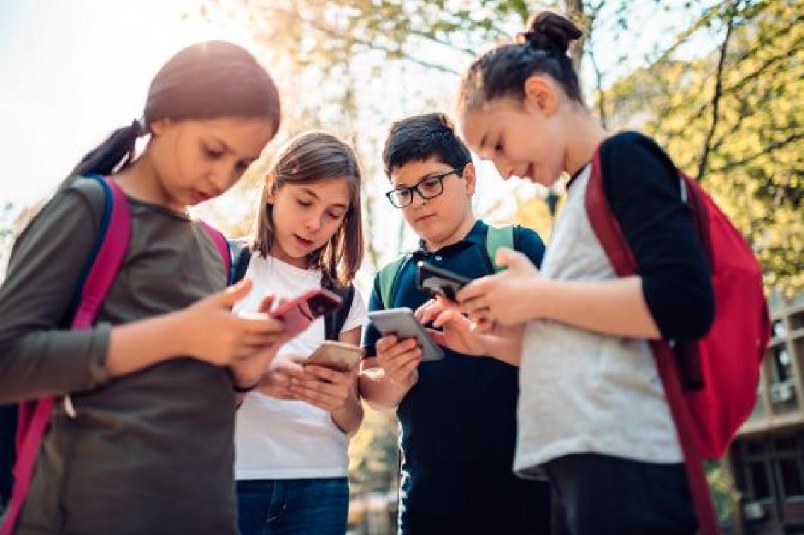 Four adolescents standing in a group, looking on their smart phones.