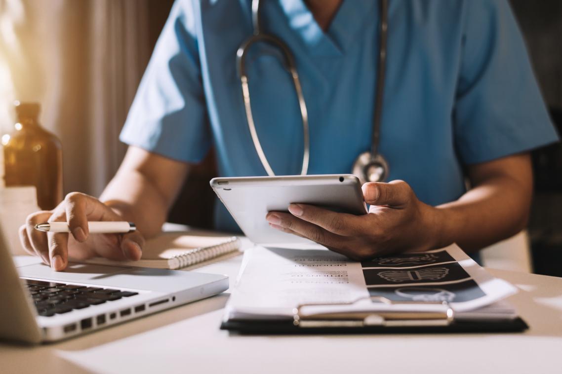 Doctor embracing digital health, working on laptop and iPad 