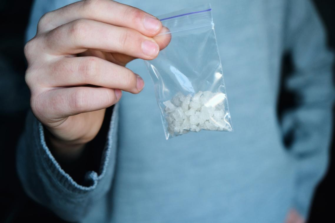 A man in a blue shirt holding a plastic bag containing white crystals.