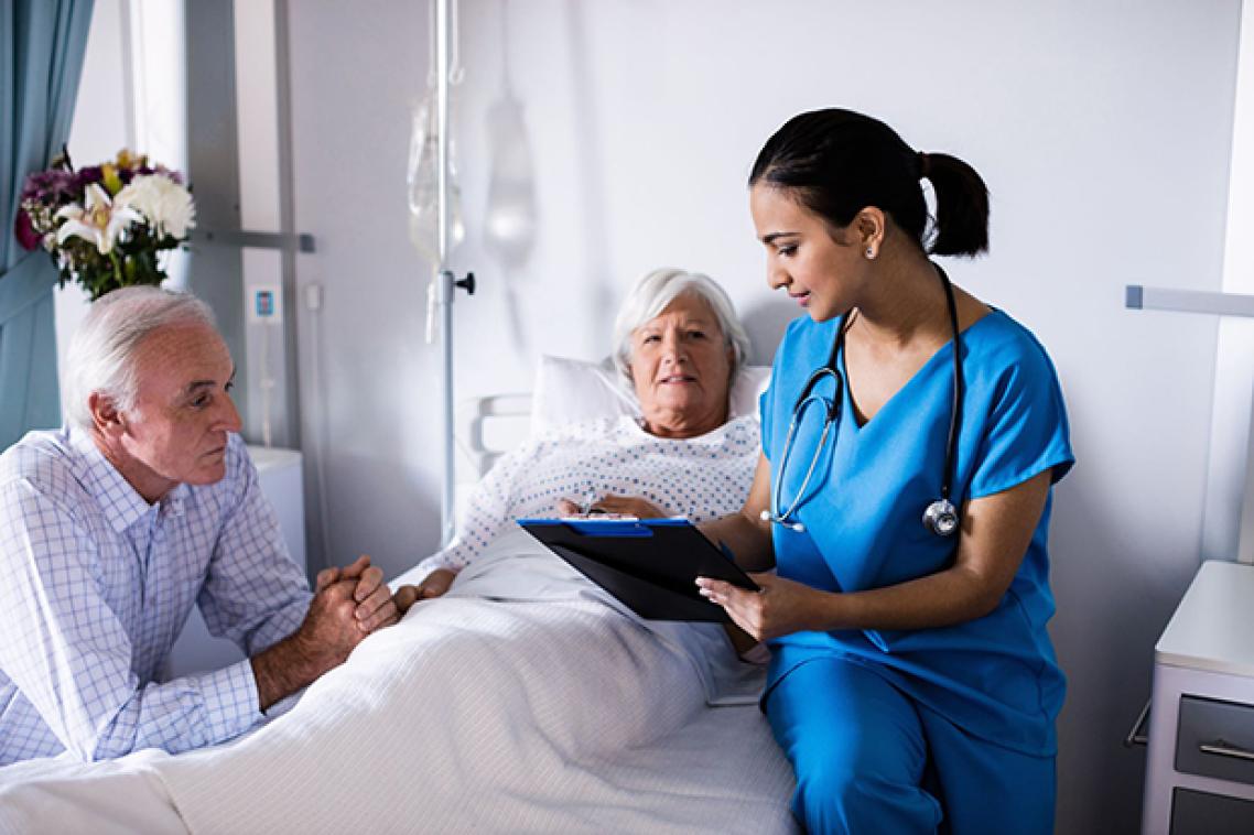 A woman in a hospital bed with a man sitting bedside and a doctor sitting on the bed.