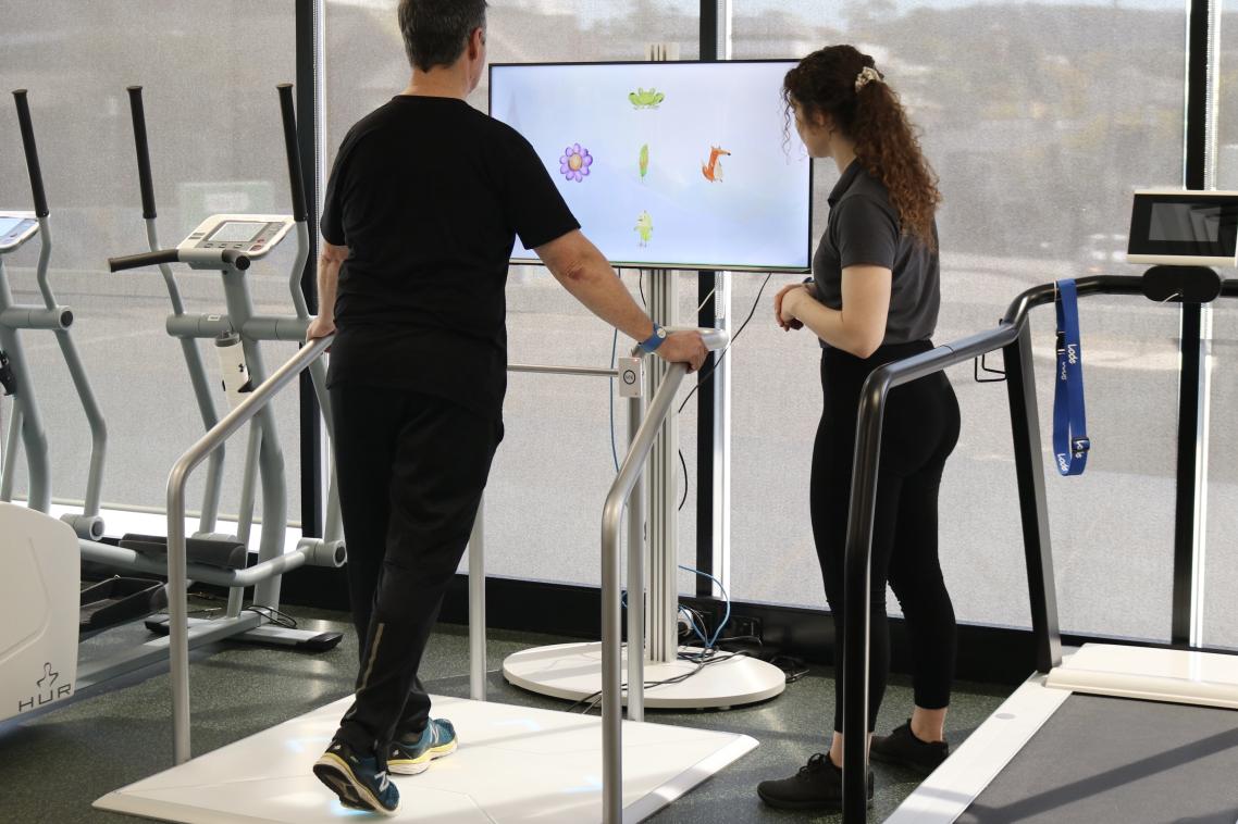 Man on exercise machine being watched by a woman