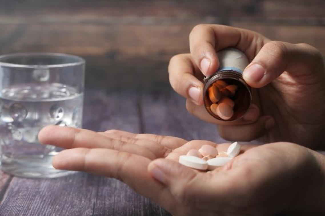 A closeup image of a hand tipping tablet medication into an open palm. There is a glass of water in the background.