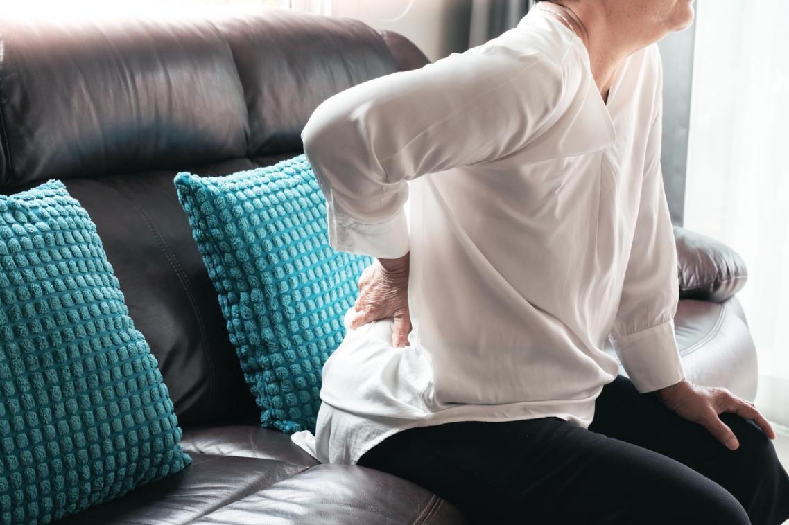 Woman leaning forward on couch with hand on lower back