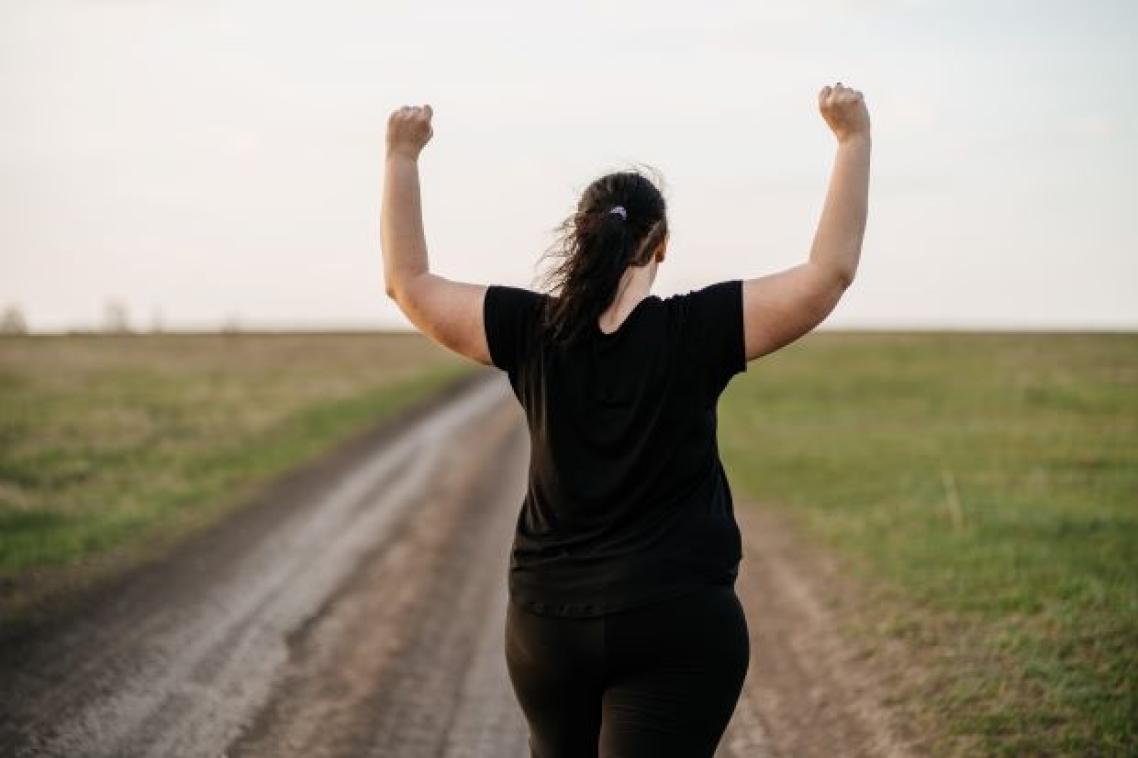 A woman with her back to the camera standing with a field with her arms raised