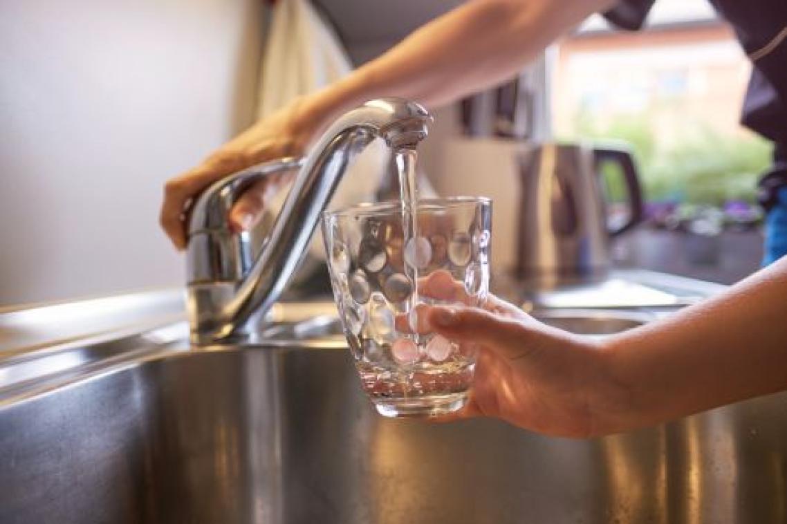 A close up a hand turning on a kitchen tap, filling a glass with water.
