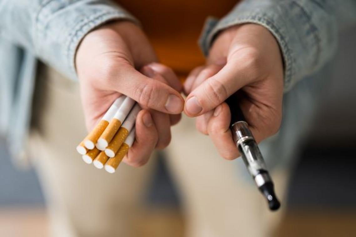 Two hands - one holding a pack of traditional cigarettes, the other holding a vape