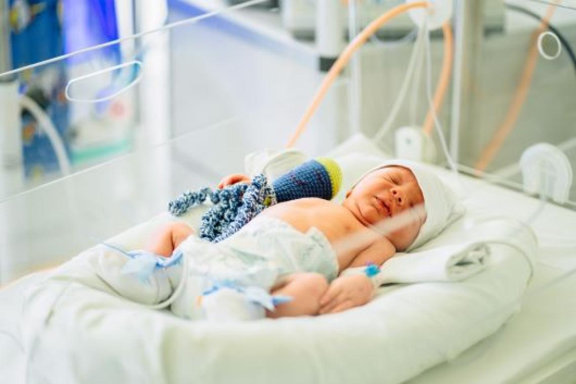 A baby in a hospital crib with tubes attached.