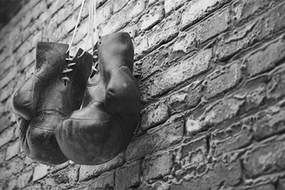 A black and white image of a pair of old leather boxing gloves hanging against a brick wall