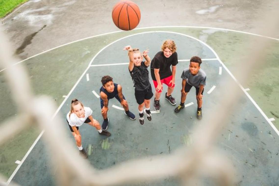 A group of teenagers standing on a basketball court in anticipation as a basketball sinks into a hoop