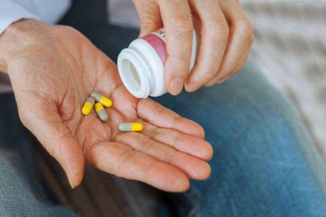 A close up photo of a hand pouring yellow and brown tablets from a white plastic pill bottle onto an open palm.