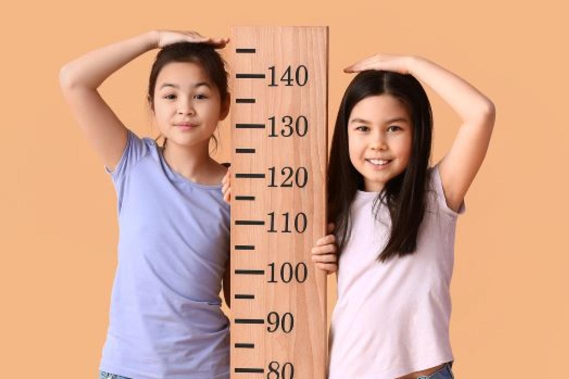 two children stand either side of a height chart