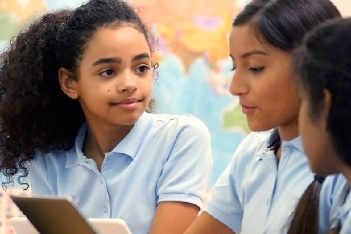 School girls sit at desk looking at iPad.